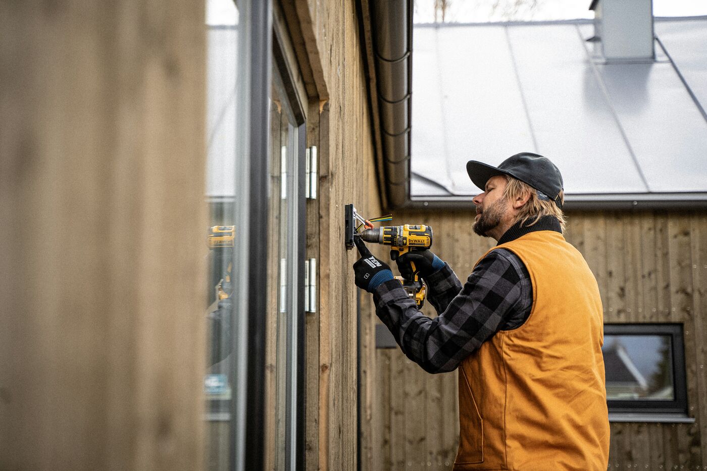 Worker using a drill beside exposed wiring in a wall-mounted electrical box