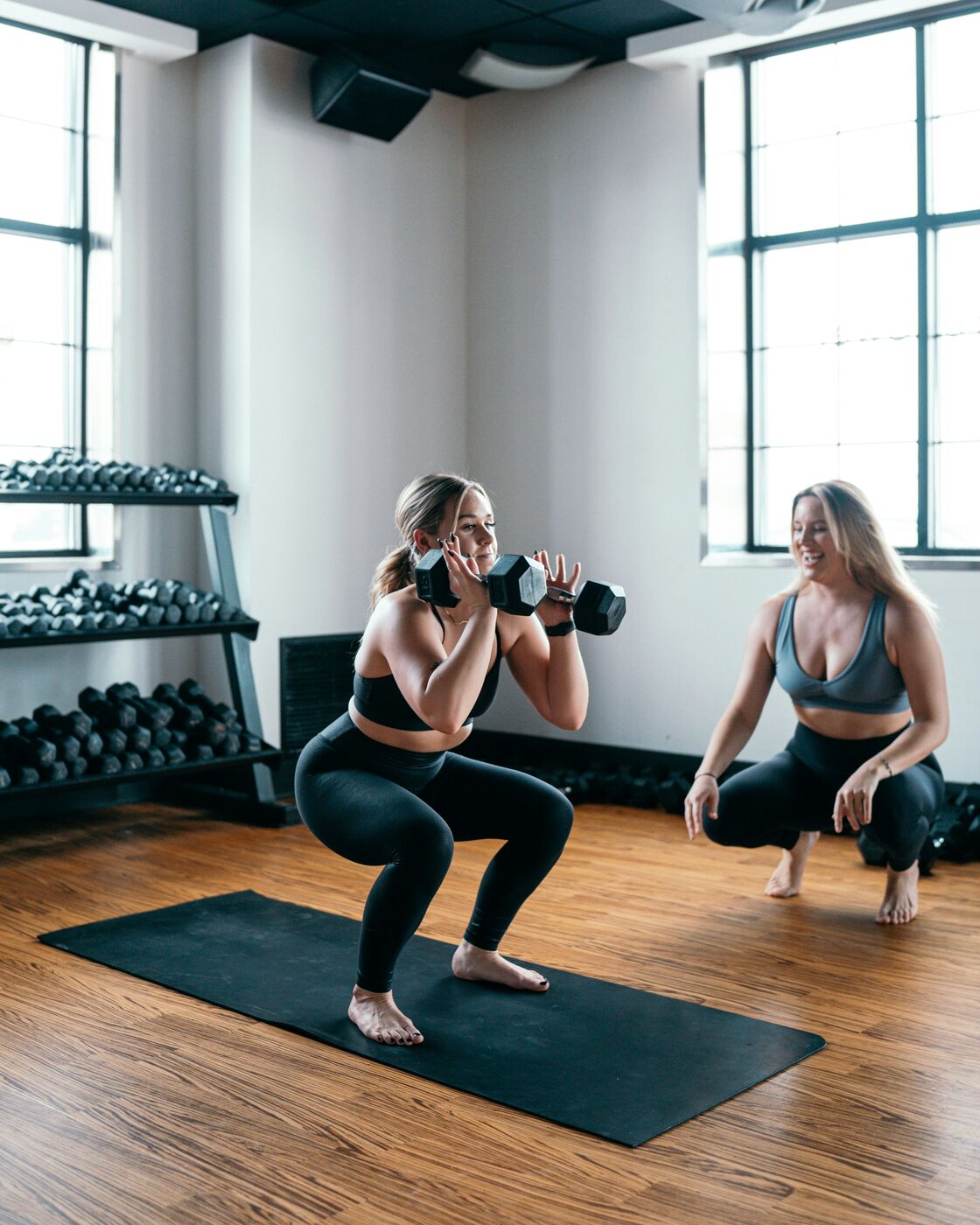 Two people practicing a dumbbell squat in a fitness studio