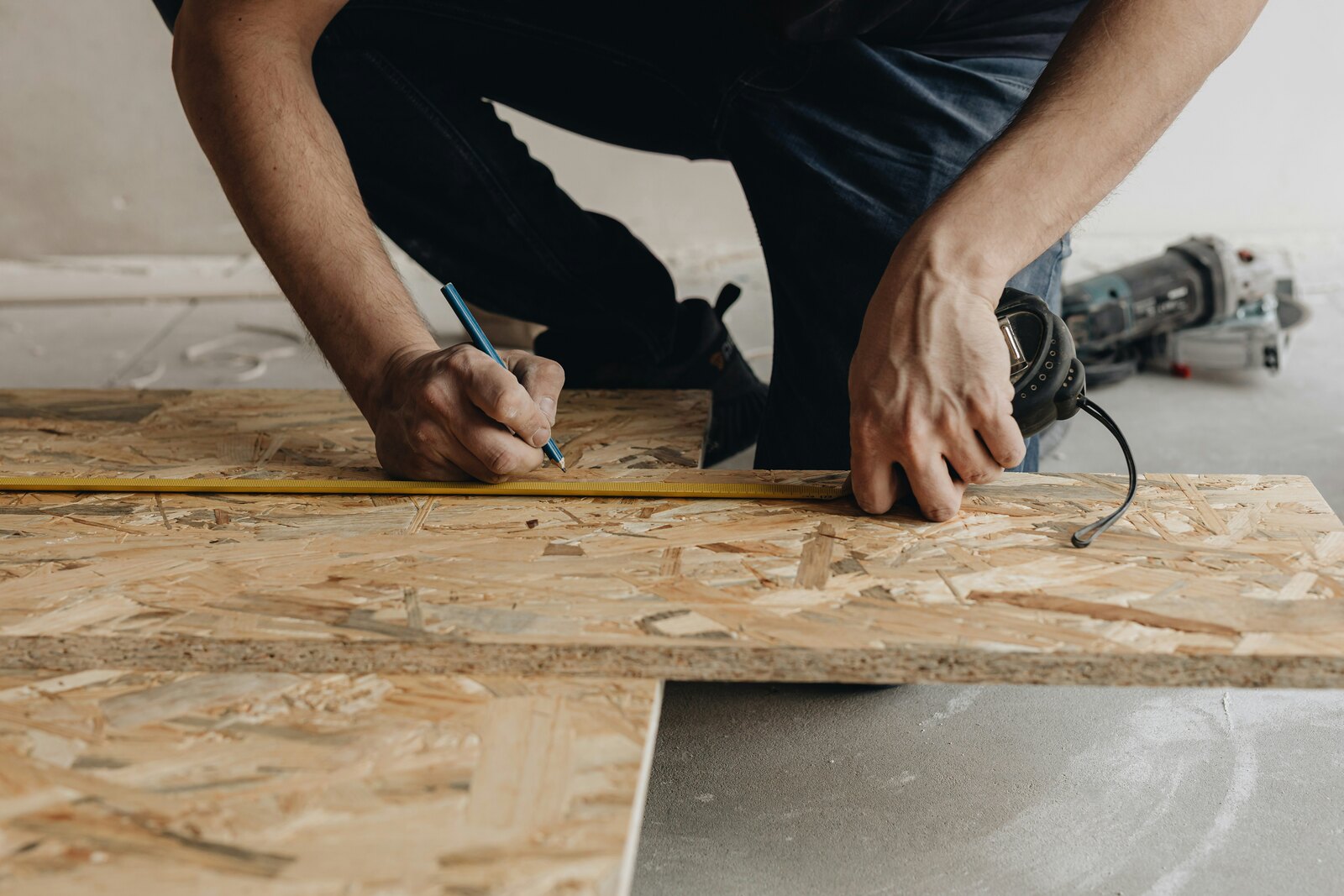 Worker measuring and marking a wood panel beside power tools