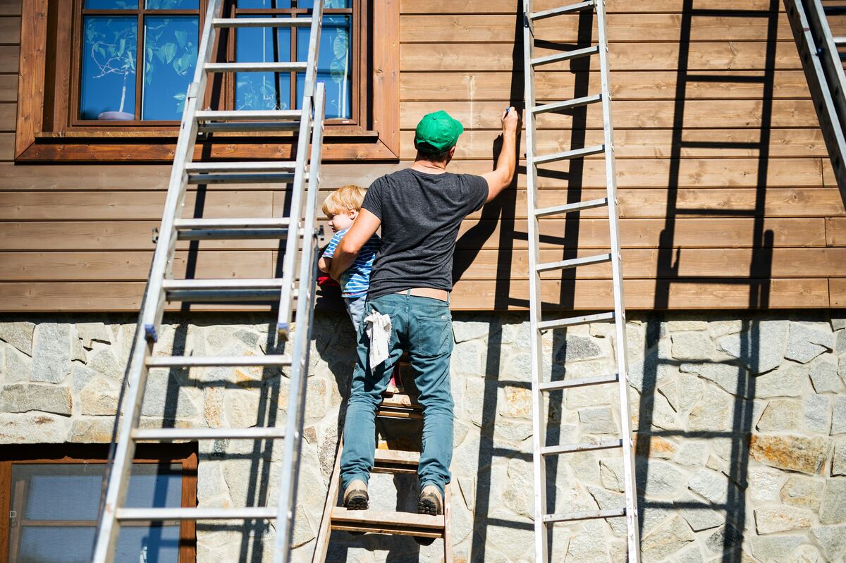 Worker on a ladder maintaining the exterior siding of a house