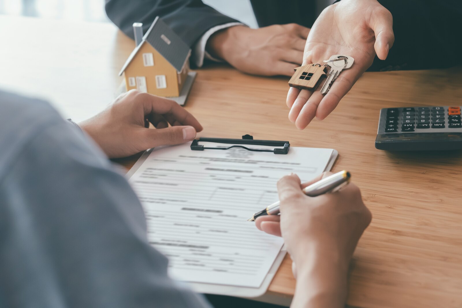 House keys being handed over beside property paperwork and a model house