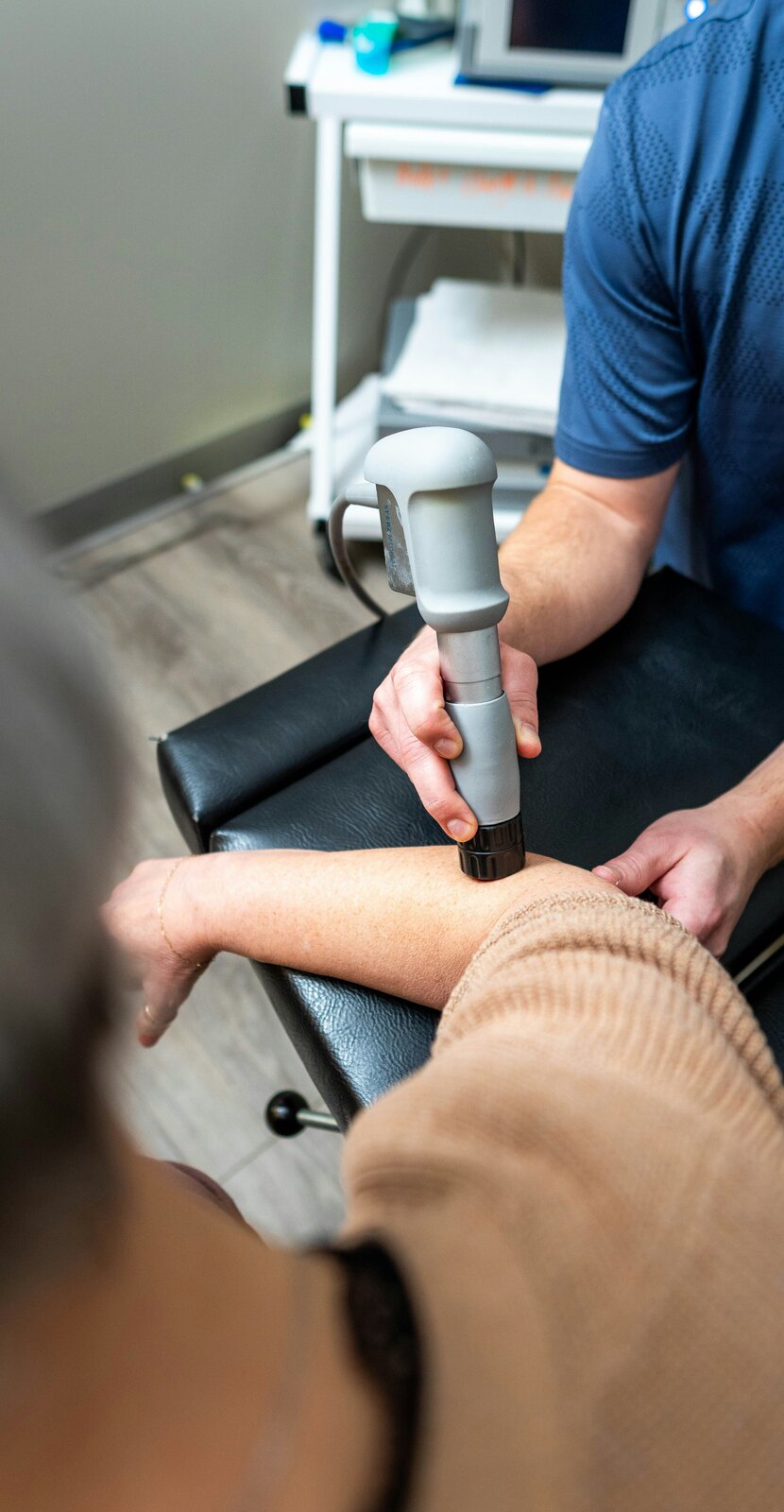 Physical therapy practitioner using a handheld device on a person’s shoulder