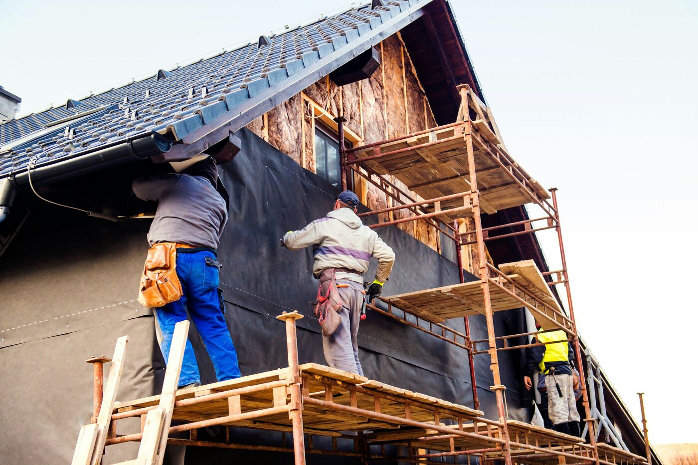 Renovation workers fitting exterior materials on scaffolding around a house