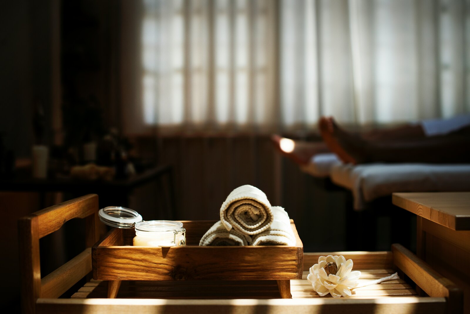 Rolled towels and a candle on a wooden tray in a softly lit spa